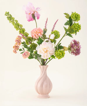 Le bouquet de fleurs artificielles en soie First Light comprend des fleurs blanches, roses, vertes et violettes avec des pétioles verts dans un vase rose pastel – un accent élégant pour n'importe quelle pièce.