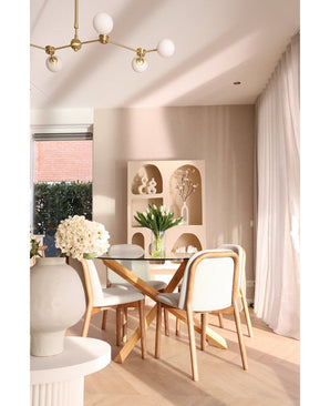 Une salle à manger moderne comprend une table ronde en verre, des chaises en bois avec des coussins blancs et le bouquet de tulipes artificielles en soie dans un vase blanc comme pièce maîtresse. Des étagères décoratives avec des vases et des rideaux transparents complètent l'espace beige.