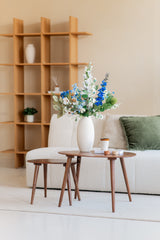 Un salon moderne avec un canapé structuré blanc, un coussin vert, des tables basses en bois et un vase blanc avec le bouquet de fleurs artificielles en soie Cool Breeze. Une planche de bois à la décoration minimaliste complète cet environnement serein.
