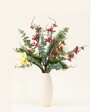 Le bouquet de fleurs artificielles en soie Midwinter Dream contient des feuilles vertes, des branches de pin, des baies rouges et des fleurs blanches dans un vase à structure blanche - parfait pour un bouquet hivernal serein sur un fond clair et uni.