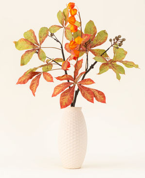 Le bouquet de fleurs artificielles en soie Autumn Flair comprend un vase avec une structure blanche et une branche de lanterne, des fleurs orange en forme de lanterne et des feuilles vert-rouge, qui forment un décor automnal élégant sur un fond clair et uni.