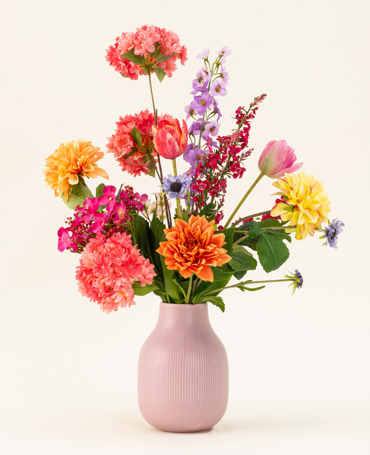 Le bouquet de fleurs artificielles en soie Colourburst Blossom comprend un vase rose pastel rempli de dahlias orange, d'œillets roses, de dahlias jaunes, de delphiniums violets et de tulipes rouges - une décoration de bouquet artificiel idéale pour n'importe quelle pièce.