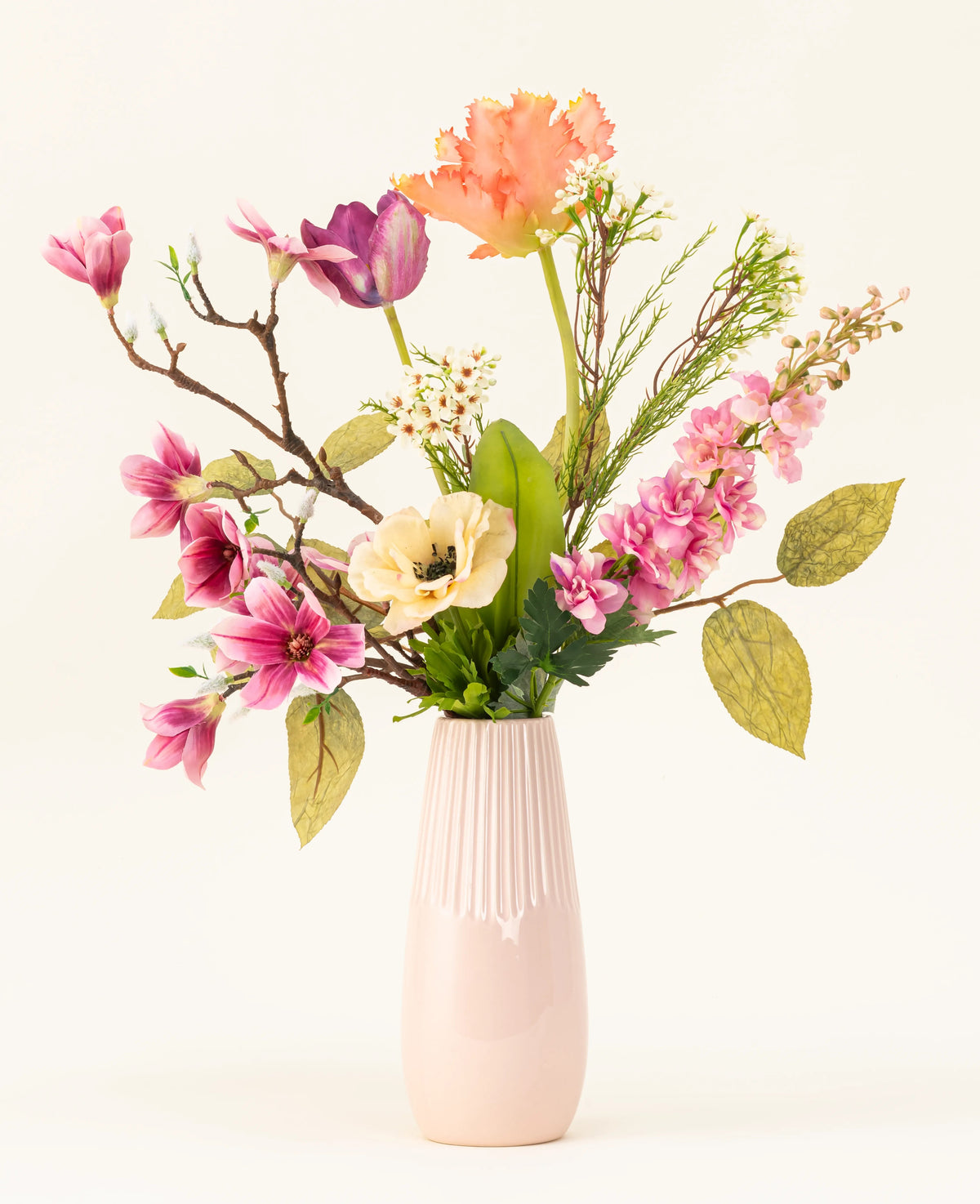 Le bouquet de fleurs artificielles en soie Spring Awakening, avec des magnolias roses, des coquelicots jaune clair et des fleurs orange et violettes dans un grand vase en céramique rose clair, met en valeur le savoir-faire hollandais sur un fond blanc uni.