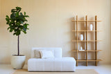 Salon minimaliste avec un canapé blanc, deux coussins et une plante artificielle Ficus Tobacco Plant Deluxe 180 cm à côté d'une étagère ouverte en bois avec des vases blancs, le tout contre un mur beige et sur un tapis clair.
