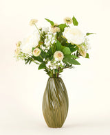 Un vase en céramique verte et nervurée contient le bouquet de fleurs artificielles en soie White Love - un arrangement de fleurs blanches et crème avec des feuilles vertes sur un fond clair uni.
