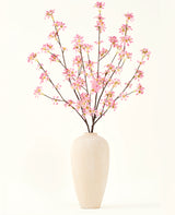 Un grand vase en céramique beige contient plusieurs branches du bouquet de fleurs artificielles en soie. Fleurs roses, avec de délicates fleurs roses et des feuilles vertes, sur un fond blanc uni.