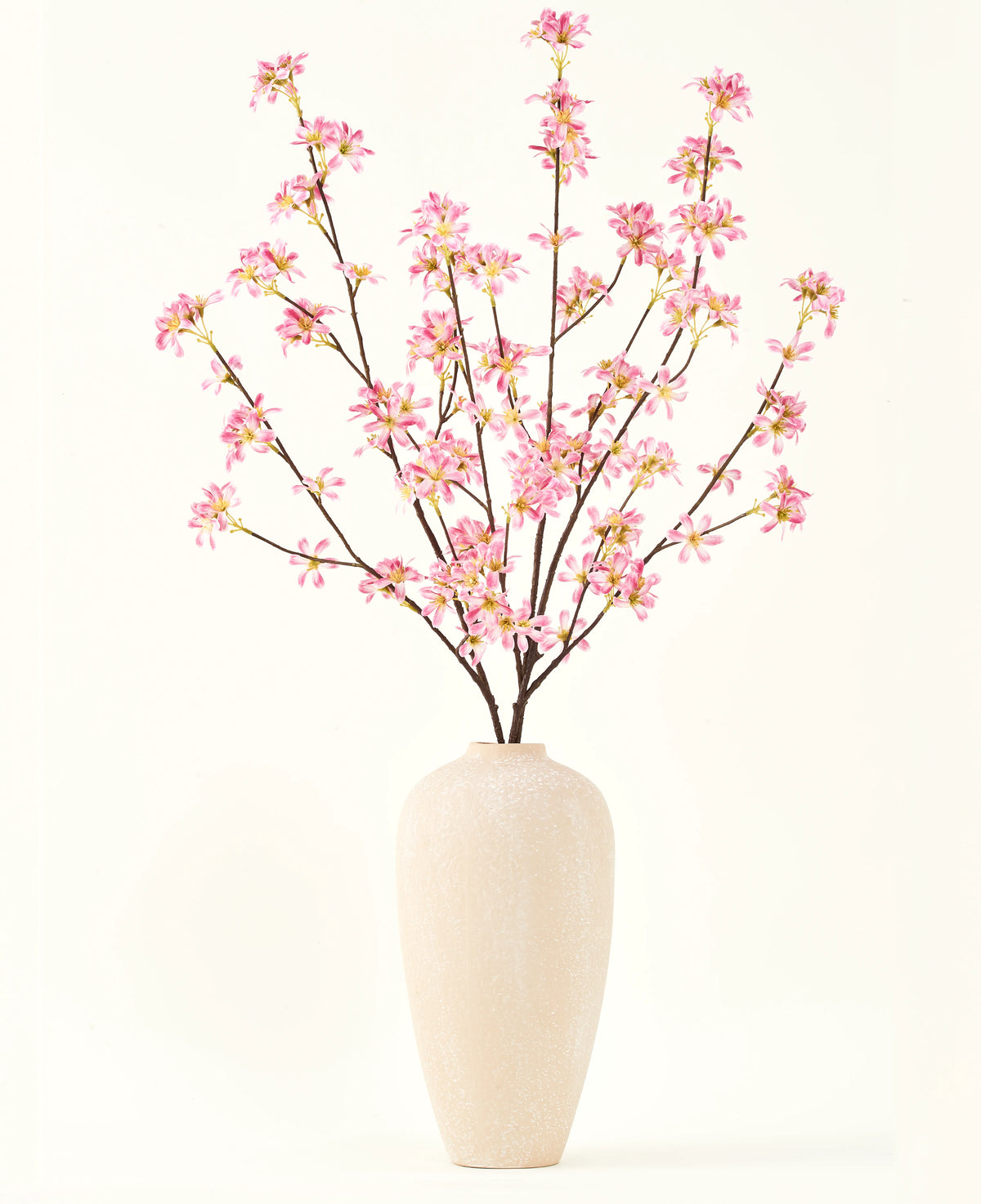 Un grand vase en céramique beige contient plusieurs branches du bouquet de fleurs artificielles en soie. Fleurs roses, avec de délicates fleurs roses et des feuilles vertes, sur un fond blanc uni.