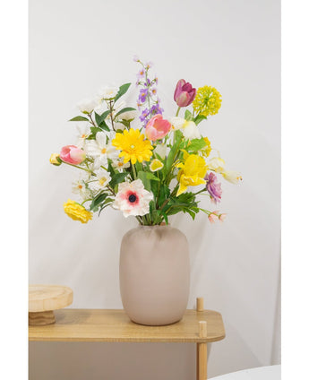 Une anémone artificielle Real Touch violette de 52 cm se dresse sur une table en bois clair et expose ses fleurs violettes réalistes dans un vase beige contre un mur blanc uni.