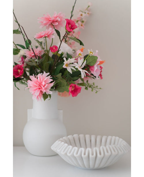 Un vase blanc avec une fleur artificielle Rhododendron Azalea 73 cm fuchsia se trouve à côté d'un bol blanc en céramique nervurée sur une surface unie sur un fond neutre.