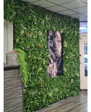 Un panneau ignifuge Kunsthaag Savanne de 100 x 100 cm avec une verdure luxuriante entoure un grand portrait facial en noir et blanc dans un espace intérieur avec des panneaux de plafond carrelés et un petit comptoir à gauche.