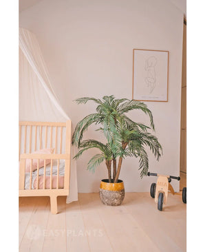 Une chambre d'enfant confortable avec un cadre de lit en bois clair, le palmier artificiel Cycas Classic 135 cm dans une jardinière jaune, un vélo jouet en bois avec le label MIA, des dessins au trait minimalistes sur le mur, du parquet en bois clair et une literie rose tendre pour plus de chaleur.