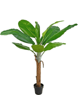 La plante artificielle bananier 150 cm possède de larges feuilles vertes vibrantes et un grand tronc marron, présenté dans un pot sur un fond blanc uni.