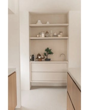 Coin cuisine minimaliste avec des étagères en bois clair avec des pots, des vases, de la décoration, un plan de travail avec du petit électroménager et la plante en pot Bonsaï Genévrier Artificiel 40 cm, ainsi que des tiroirs intégrés et un petit robinet, le tout dans des tons neutres.