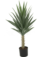 La plante artificielle Yucca 100 cm UV a de hautes feuilles vertes épineuses sur une tige épaisse, est mise en pot dans un petit pot noir avec de la terre et est photographiée sur un fond blanc.