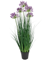 Le pot d'herbe d'oignon d'agapanthe violette d'herbe artificielle est une plante artificielle ignifuge de 90 cm de haut avec de longues feuilles vertes et des bouquets de fleurs violettes, présentées dans un pot noir uni sur un fond blanc.