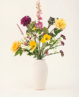 Le bouquet de fleurs artificielles en soie Daisy Daydream comprend un vase texturé blanc et un mélange vibrant de fleurs jaunes, roses, violettes et blanches avec des feuilles vertes, ajoutant une beauté durable à tout fond clair uni.