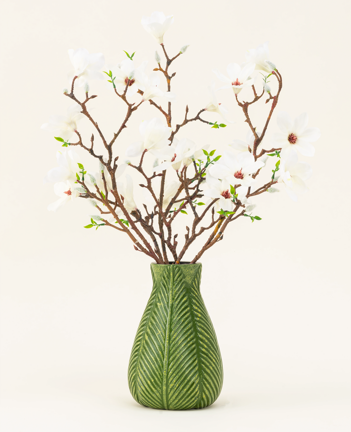 Un vase vert montre le bouquet de fleurs artificielles en soie Magnolia blanc, avec plusieurs branches de magnolia blanches avec de petites feuilles vertes, sur un fond clair uni.