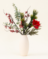 Le bouquet de fleurs artificielles en soie Winterberry Bliss comprend des baies rouges, des branches de pin, de l'eucalyptus, de l'amaryllis rouge et des pommes de pin dans un vase texturé blanc - idéal pour la décoration de Noël ou pour exposer sur un fond clair.