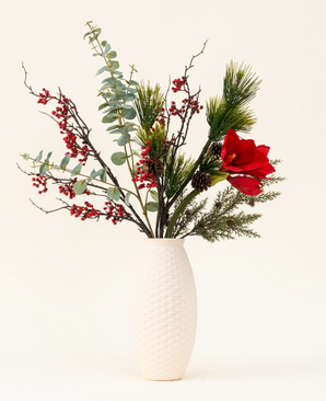 Le bouquet de fleurs artificielles en soie Winterberry Bliss comprend des baies rouges, des branches de pin, de l'eucalyptus, de l'amaryllis rouge et des pommes de pin dans un vase texturé blanc - idéal pour la décoration de Noël ou pour exposer sur un fond clair.
