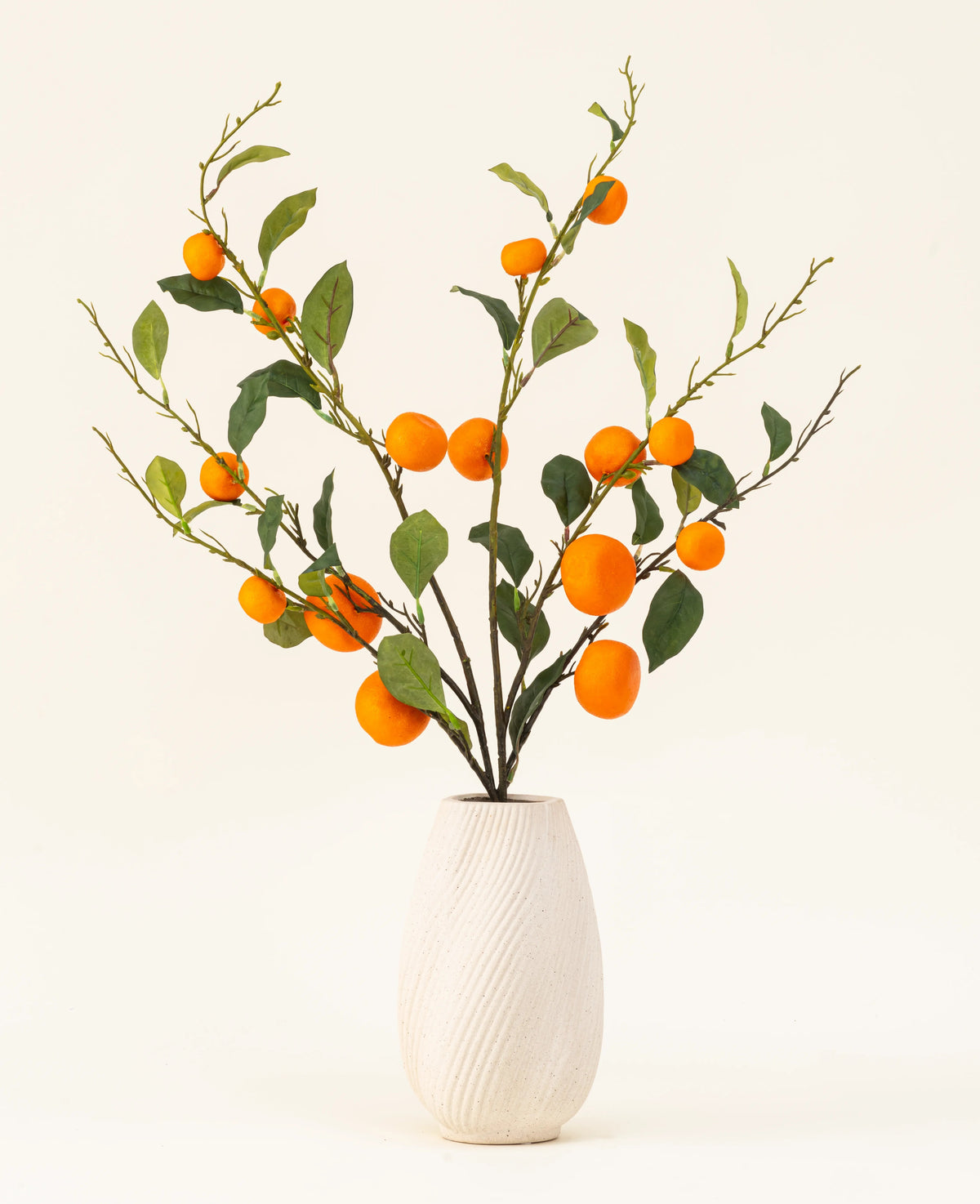 Le bouquet de fleurs artificielles en soie Mandarin a un vase texturé blanc et des branches de feuilles vertes et de mandarines artificielles orange vif, qui ajoutent une touche vivante sur un fond clair uni.