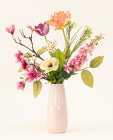 Le bouquet de fleurs artificielles en soie Spring Awakening, avec des magnolias roses, des coquelicots jaune clair et des fleurs orange et violettes dans un grand vase en céramique rose clair, met en valeur le savoir-faire hollandais sur un fond blanc uni.