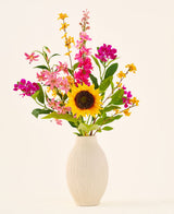 Le bouquet de fleurs artificielles en soie 'Tiny Sunshine' est placé dans un vase en céramique beige, composé d'un bouquet de fleurs artificielles réalistes, comme un grand tournesol, des fleurs roses et magenta et des fleurs jaunes avec des feuilles vertes, sur un fond clair uni. Cet arrangement d'Easyplants se compose de belles fleurs en soie qui ajoutent une beauté durable à n'importe quelle pièce.