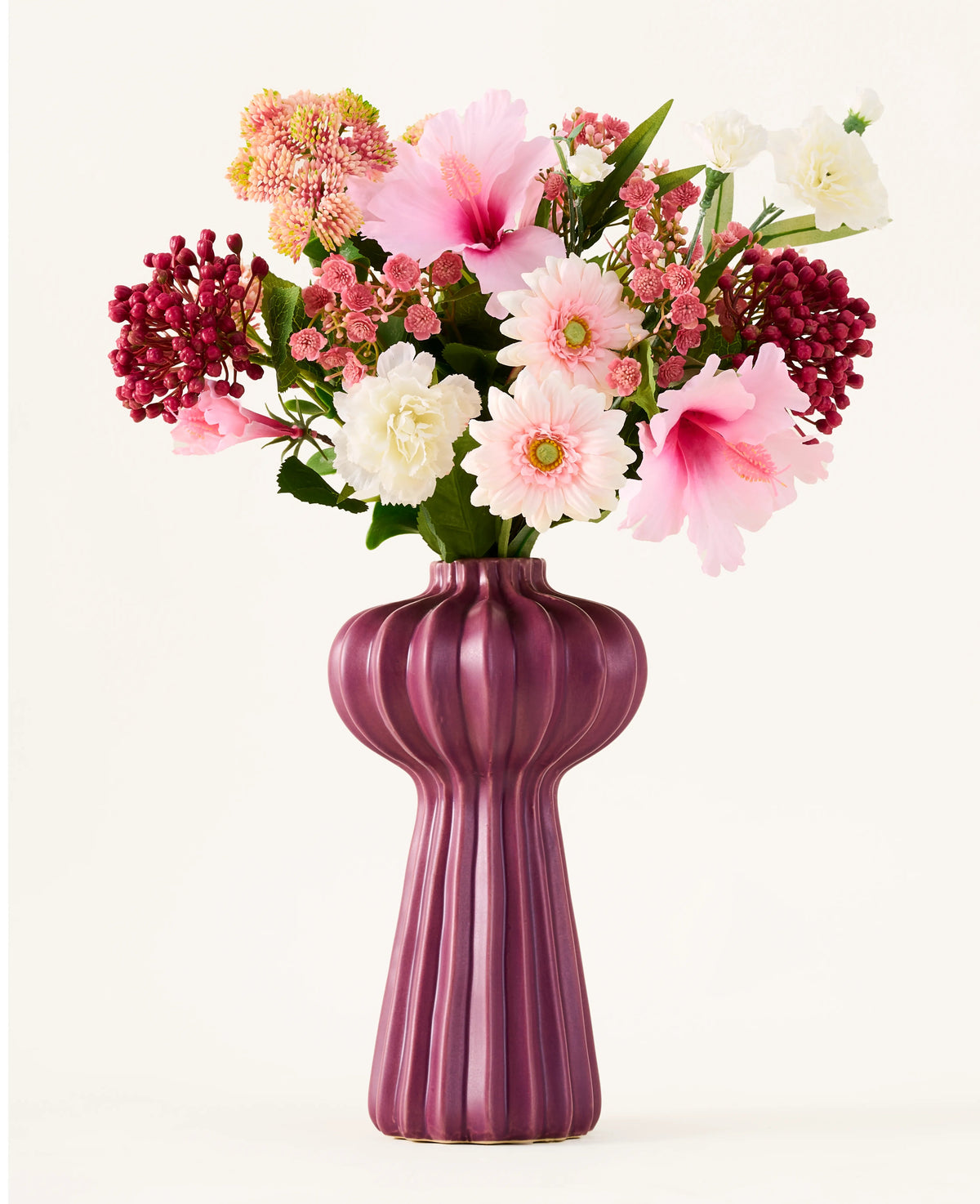 Un bouquet de fleurs artificielles de Zijden, « Bloom & Berry », avec des fleurs artificielles roses, blanches et rouges, est magnifiquement disposé dans un grand vase violet nervuré sur un fond blanc uni.