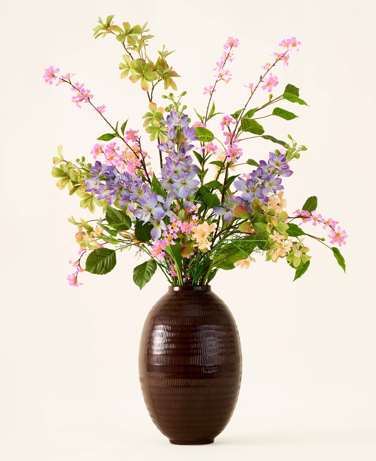 Dans un vase marron foncé se trouve un bouquet de fleurs artificielles en soie roses, violettes et jaunes, le bouquet « Sky Kiss », avec des feuilles vertes, sur un fond uni clair. Cette décoration sans entretien apporte une beauté durable à n'importe quelle pièce, sans nécessiter d'entretien.