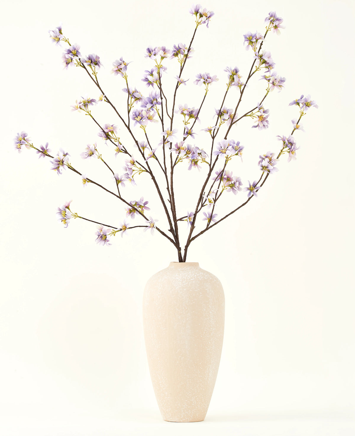 Un grand vase en céramique de couleur crème contient un certain nombre de fines branches avec le texte Bouquet de fleurs artificielles en soie Branche de fleurs artificielles violette, sur un fond uni et clair.