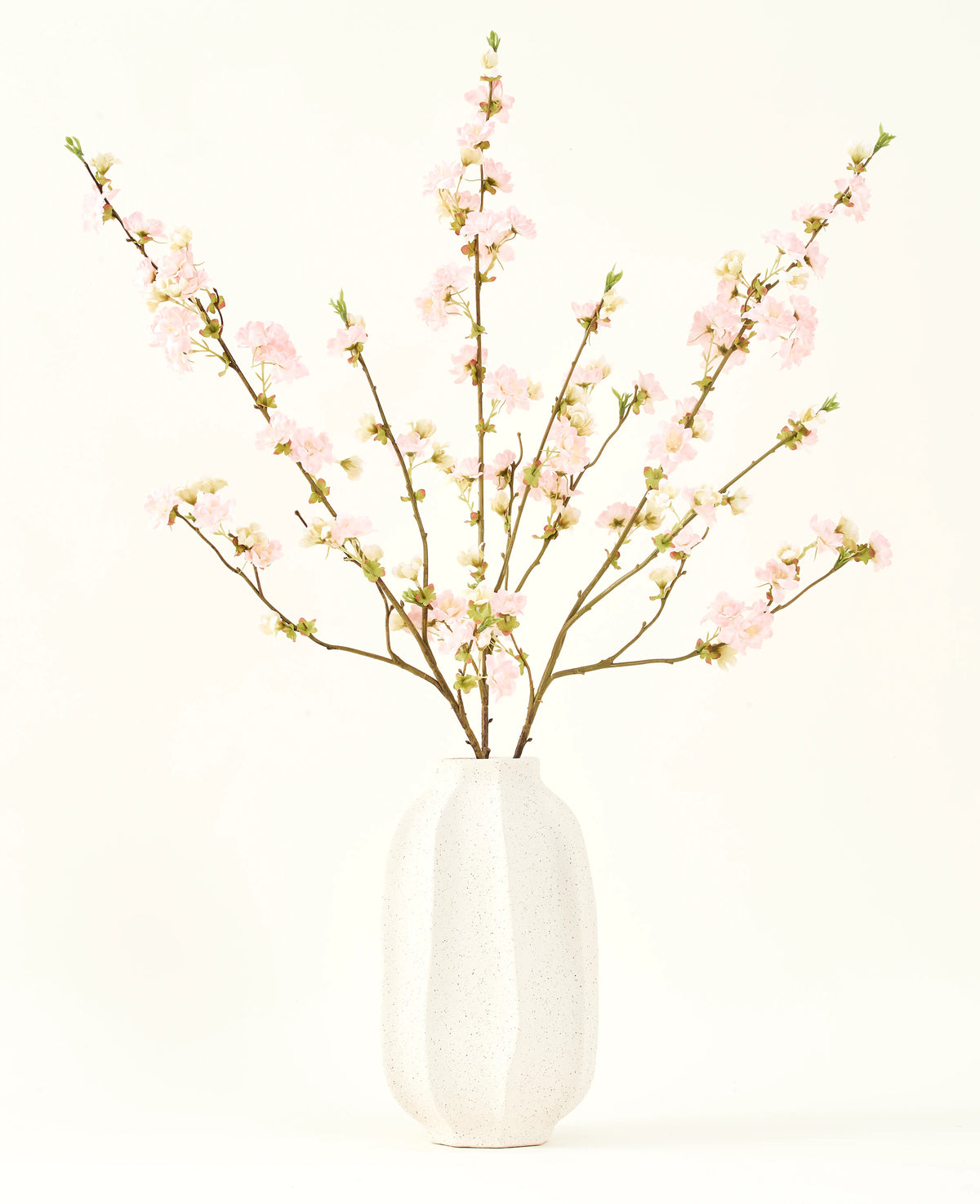Le bouquet de fleurs artificielles en soie Fleur de cerisier rose clair 94 cm présente de délicates fleurs de cerisier artificielles roses dans un vase en céramique blanche, qui ajoute de l'élégance sur un fond clair et uni.