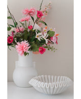 Un vase blanc avec une fleur artificielle Rhododendron Azalea 73 cm fuchsia se trouve à côté d'un bol blanc en céramique nervurée sur une surface unie sur un fond neutre.