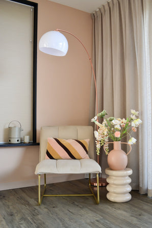 Un coin moderne et cosy avec une chaise couleur crème avec un coussin rayé, un lampadaire haut en forme d'arc, des rideaux beiges, un parquet et un vase rond avec des fleurs artificielles Fritillary 94 cm blanches sur une table d'appoint sculptée.