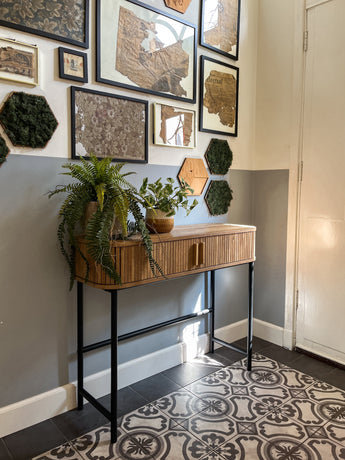 Un hall avec du carrelage à motifs, une console en bois avec la plante artificielle Golden Vine en pot de 25 cm et une galerie murale avec des cartes encadrées et de l'art de mousse hexagonale sur un mur bicolore gris et blanc.