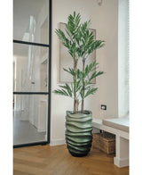 La plante artificielle Parlour Deluxe 120 cm a des tiges fines et de longues feuilles vertes dans un vase vert ondulé, parfait pour les pièces modernes et lumineuses avec des parquets en bois clair et de grandes fenêtres.