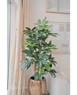 La plante artificielle Schefflera de 150 cm aux larges feuilles vertes se trouve dans un pot doré à côté d'un canapé crème et de rideaux lumineux, tandis que des œuvres d'art abstraites sont accrochées au mur.