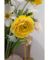 Un gros plan de la renoncule artificielle Real Touch Yellow 60 cm, une renoncule artificielle jaune vif avec des pétales superposés, adaptée dans un vase d'intérieur à côté de fleurs blanches et rose clair.