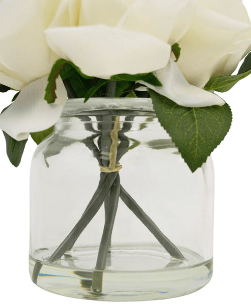 Gros plan du Bouquet de Roses Artificielles Real Touch Blanc 18cm : fleurs artificielles blanches aux feuilles vertes dans un pot en verre transparent, tiges visibles maintenues ensemble par un élastique.