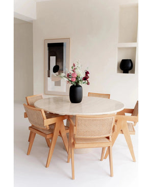 Une table ronde en marbre avec quatre chaises en bois entoure le Vase Artic Noir Ø21 x H29 cm rempli de fleurs. Des œuvres d'art murales abstraites et une pièce de décoration noire sur une étagère intégrée complètent la pièce minimaliste aux tons clairs.
