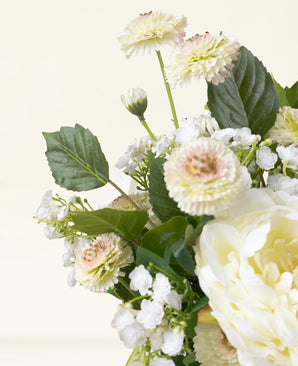 Un gros plan du bouquet de fleurs artificielles en soie White Love, avec des fleurs artificielles jaune clair et blanches avec des feuilles vertes sur un fond crème clair.