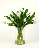 Le bouquet artificiel en soie Tulipes dans un vase Blanc présente des tulipes blanches avec des feuilles et des tiges vertes dans un vase en verre transparent, sur un fond clair simple.