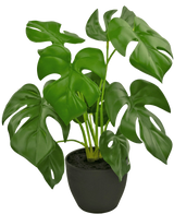 Le Monstera artificiel 40 cm en pot décoratif noir est un Monstera artificiel avec de grandes feuilles vertes brillantes avec des trous et des fissures naturelles, dans un simple pot décoratif noir rempli de terre sombre.