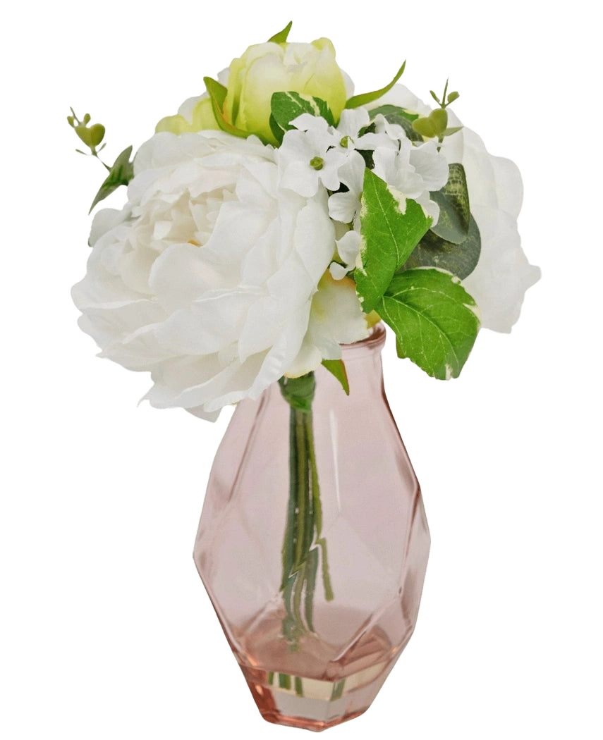 Le Bouquet Artificiel en Verre 25 cm présente un petit bouquet de fleurs blanches aux feuilles vertes, disposées dans un vase en verre rose clair facetté.