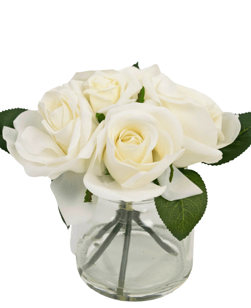 Le Bouquet de Roses Artificielles Real Touch Blanc 18 cm est un petit vase en verre transparent avec des roses blanches réalistes et des feuilles vertes, sur un fond blanc uni.
